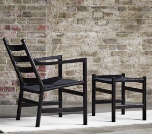 Black wicker outdoor chair and matching wicker ottoman in front of brick wall