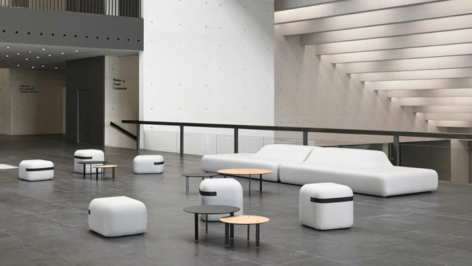 Open loft style work space with modern white couches, different sized white and black stools with black and tan round tables.