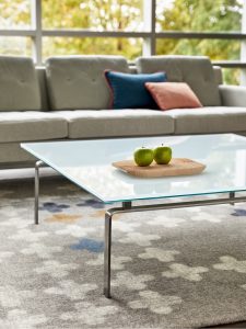 Glass coffee table on grey patterned carpet with grey midcentury modern sofa