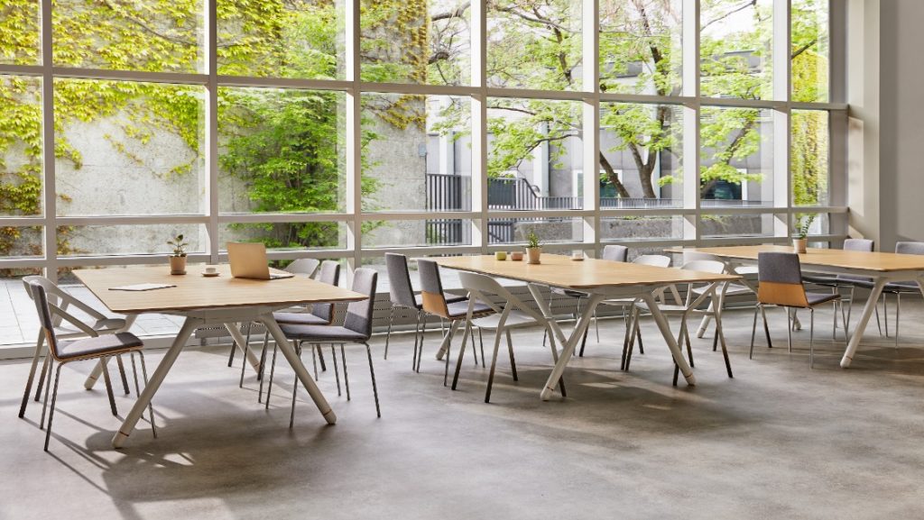 Open concept collaborative space with floor to ceiling windows, three large wooden conference tables, grey office chairs and concrete floors