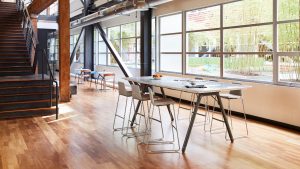 Open concept, industrial style workspace with tall metal table, brown bar stools and hardwood floors