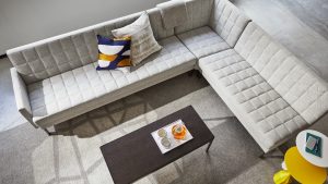 Grey office sectional couch in lounge space with wooden office table and grey carpeting