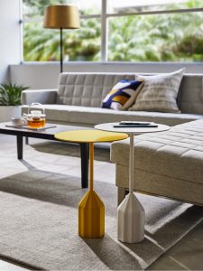 Yellow and white side tables in an office lounge space with grey sectional couch, wooden table, grey rug, and large glass windows