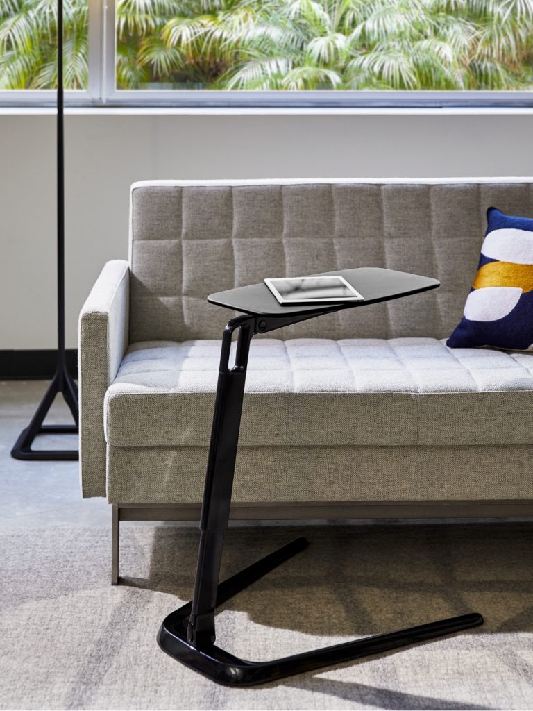 Half of light grey office lounge couch with side table, tablet, and standing lamp