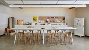 Long white collaborative table with wooden stools inside office meeting area