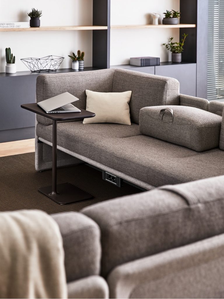 Grey corner sectional couch in lounge space with connected power outlet and nearby side table