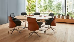 Round office meeting table surrounded by matching leather-back armchairs in front of window