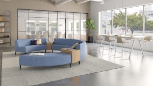 Blue round office sectional couch with white rug and nearby cafe-height table in office lounge setting