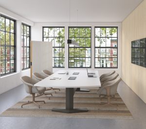 Office meeting room with long white table, mid-backed upholstered chairs, mobile whiteboard, and monitor on nearby wall