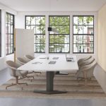 Office meeting room with long white table, mid-backed upholstered chairs, mobile whiteboard, and monitor on nearby wall
