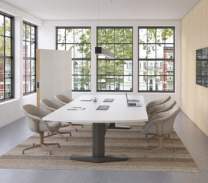 Office meeting room with long white table, mid-backed upholstered chairs, mobile whiteboard, and monitor on nearby wall