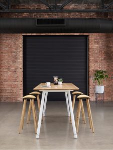 Wooden conference table with matching wooden rounded-seat stools in an industrial office meeting room with garage door