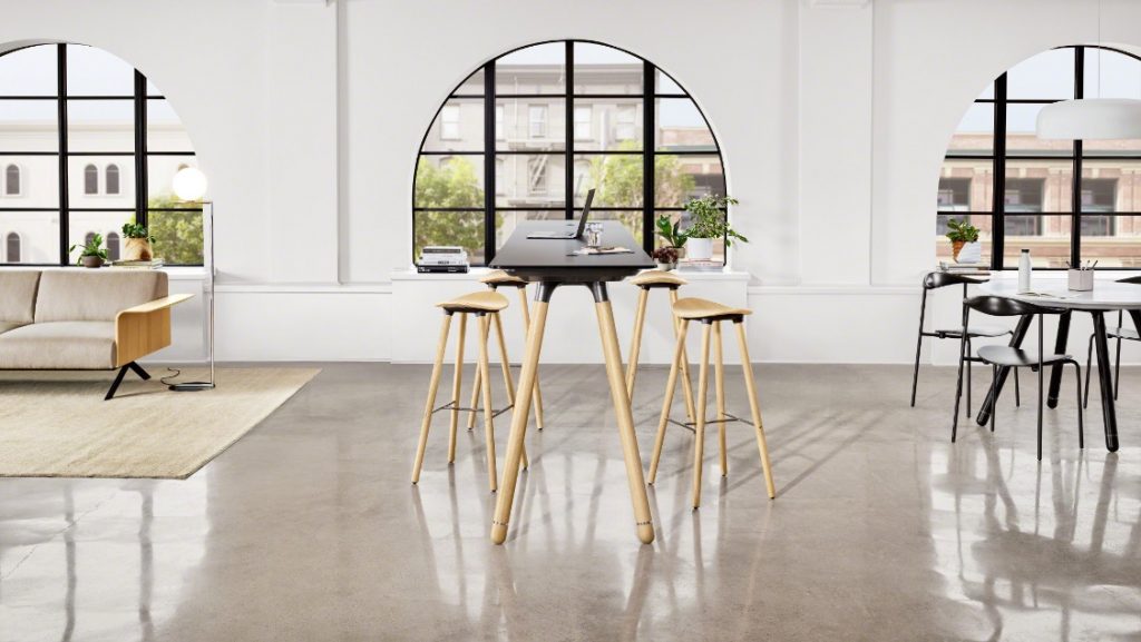 Long grey office conference table with wooden legs and matching stools in front of an arched window