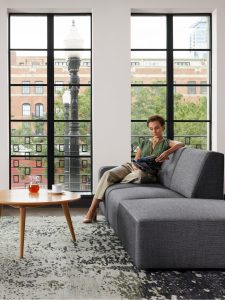 Woman in office relaxing on sofa reading magazine in front of window walls facing street