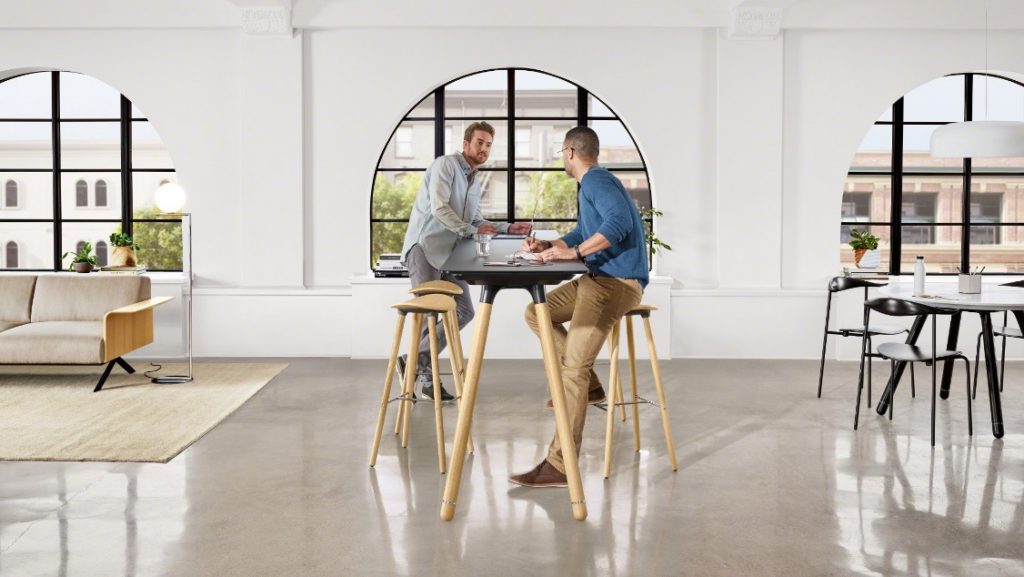 Two office workers sitting at collaborative space on wooden stools with long table