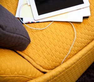 Textured orange fabric on office sofa with grey pillow and plugged in iPad tablet
