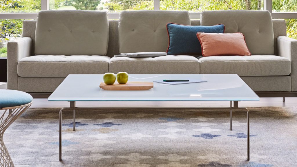 Glass top coffee table on grey patterned rug with grey office couch nearby