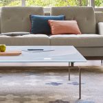 Glass top coffee table on grey patterned rug with grey office couch nearby