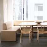 Beige together bench next to a dinning table, surrounded by four chairs.