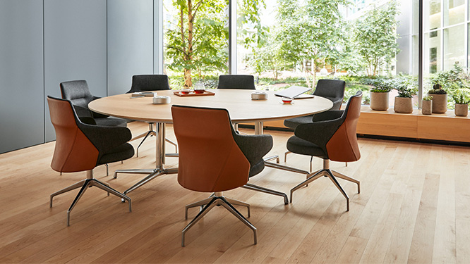 Round office meeting table surrounded by matching leather-back armchairs in front of window