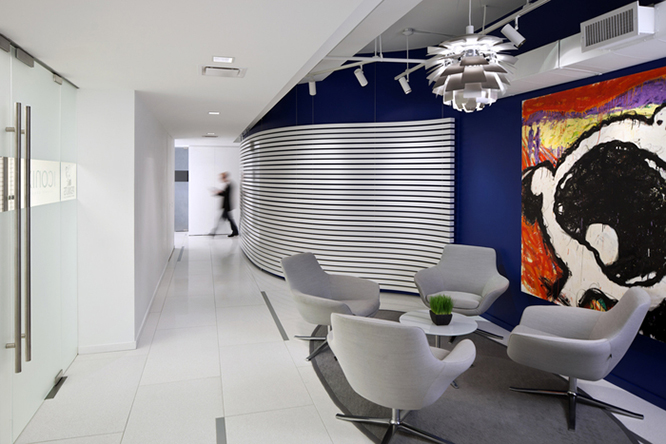 Small white table surrounded by grey lounge chairs on a circular dark grey rug, dark blue walls and a giant painting