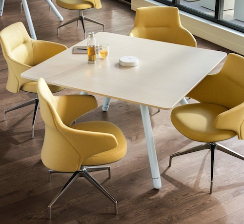 Square, light brown wooden table with yellow lounge office chairs 