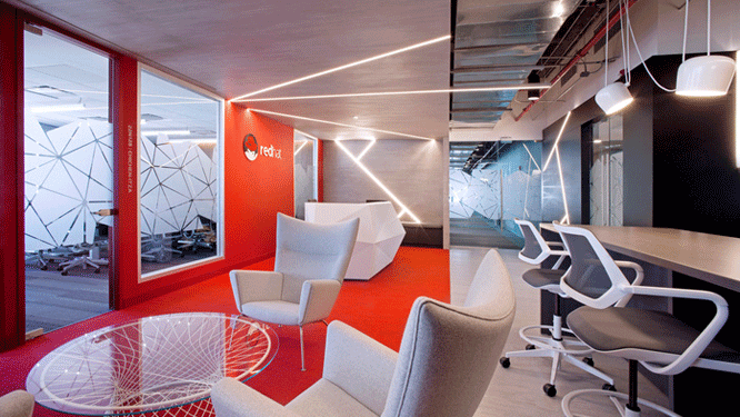 Collaborative work space with red walls, red carpet, glass top coffee tables and light grey lounge seats.