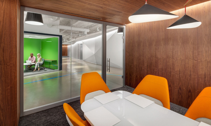 Enclosed conference room with white rectangular table, orange office chairs and interior glass windows and door looking out into a hallway
