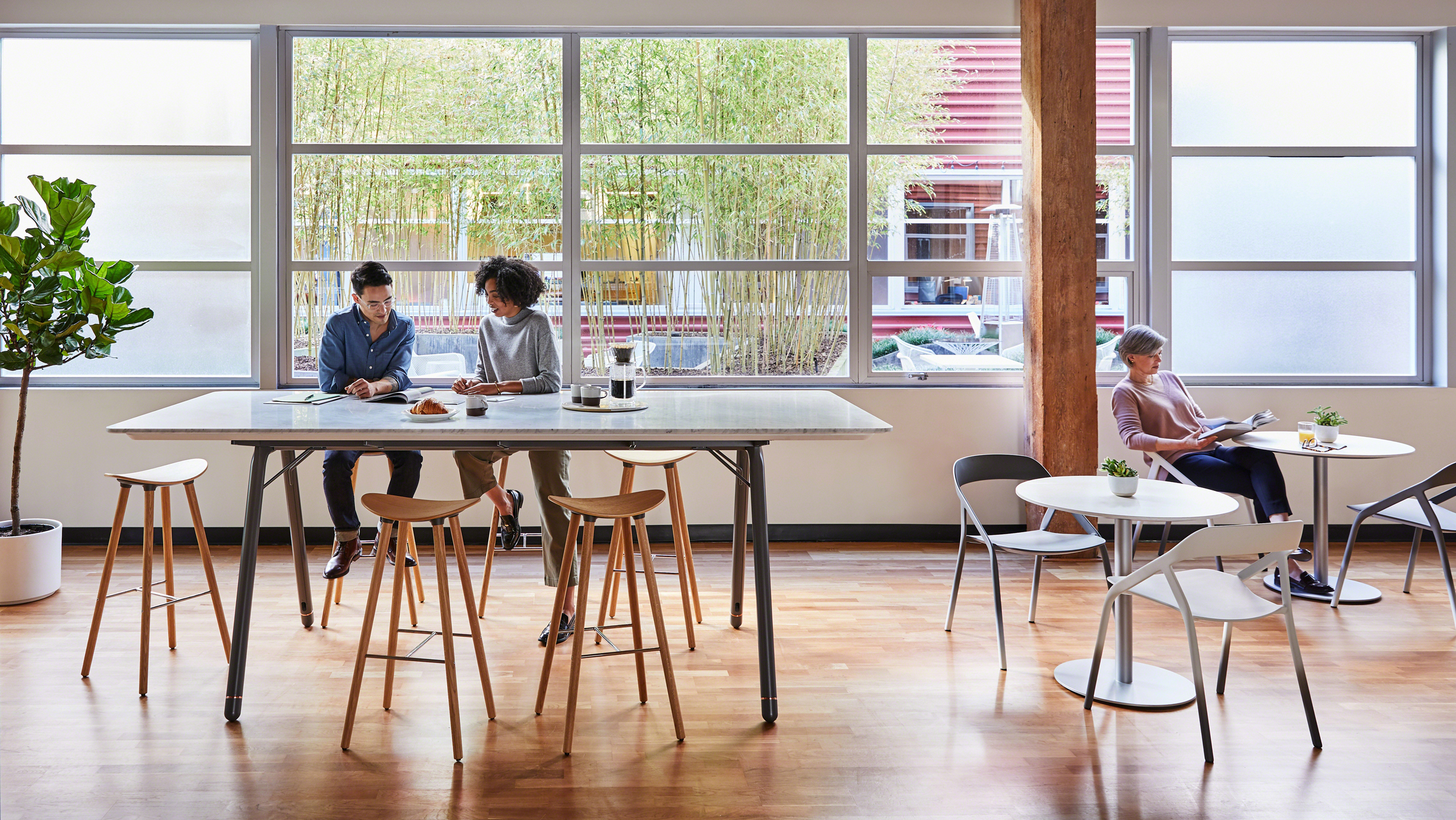 Two team members collaborate in cafe meeting space at standing-height table and wood stools