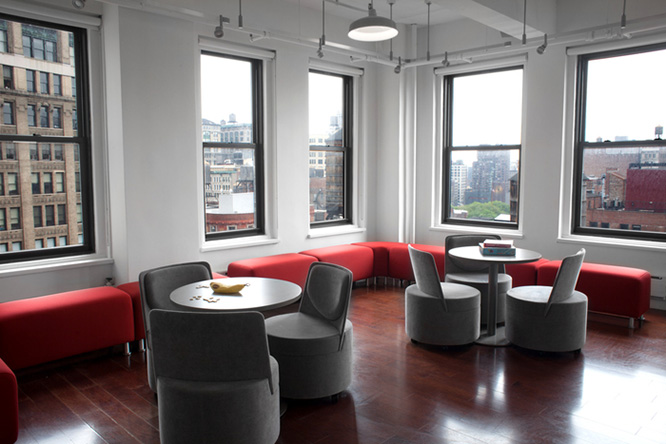Two round metal tables with black round chairs in a room with dark hardwood floors and windows overlooking the city