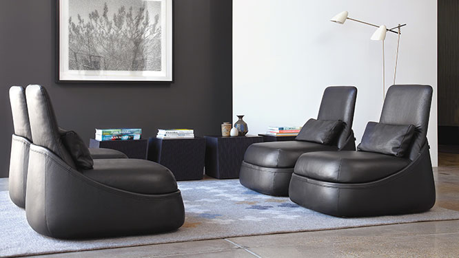Four black leather lounge seats facing each other on top of light grey rug with dark blue cube side tables.