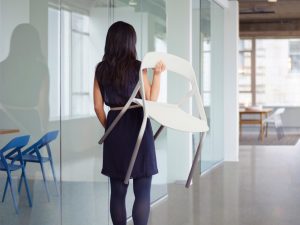 Young woman carrying white carbon fiber side chair through office