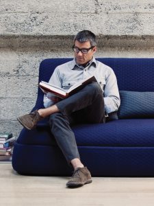 Man reading a book and sitting on dark blue Hosa sofa with blue matching pillows