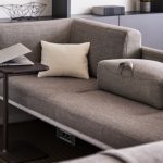 Corner seat of grey office sectional with round table for laptop, charging ports, and low armrest