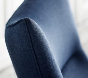Corner of wing-back office chair with blue upholstery and stitching detail
