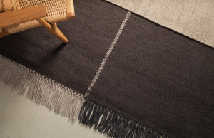 Grey carpeting with contrasting stitching and two-tone fringe with woven wicker lounge chair