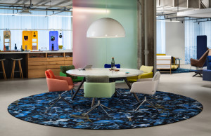 Colorful office collaborative space with round coffee table, colorful square chairs around table, and blue patterned rug