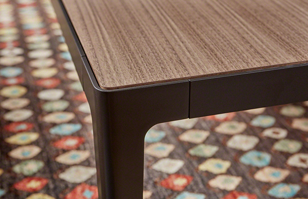 Close up of the corner of a wooden coffee table with wooden top and dark metal legs.