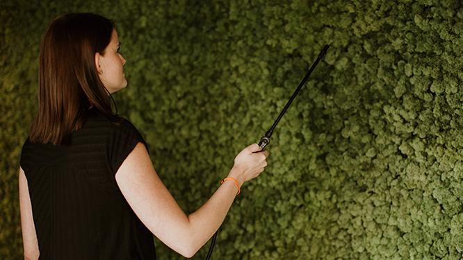 Woman using mister to water moss covered decorative wall.