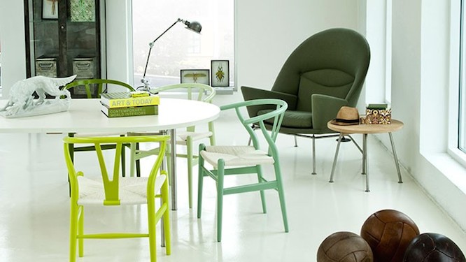 White round table with small chairs in different shades of green, a dark green lounge chair in the background next to a small round wooden side table.