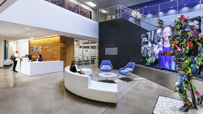 Reception area with large white couch, large screen TV, two blue lounge chairs and small, round white coffee table.