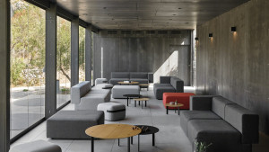 Monochromatic design office lounge with wooden tables, grey couches, and red bench