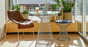 Balcony cafe space overlooking city with outdoor metal furniture, brown leather chair, coffee, and open laptop on table