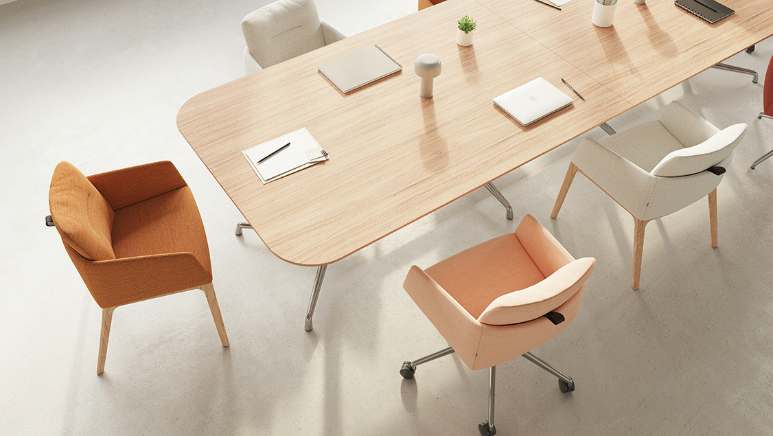 A rectangular wooden table with rounded corners, surrounded by four marien chairs. The table holds two closed laptops, a notebook, and a small cylindrical object.