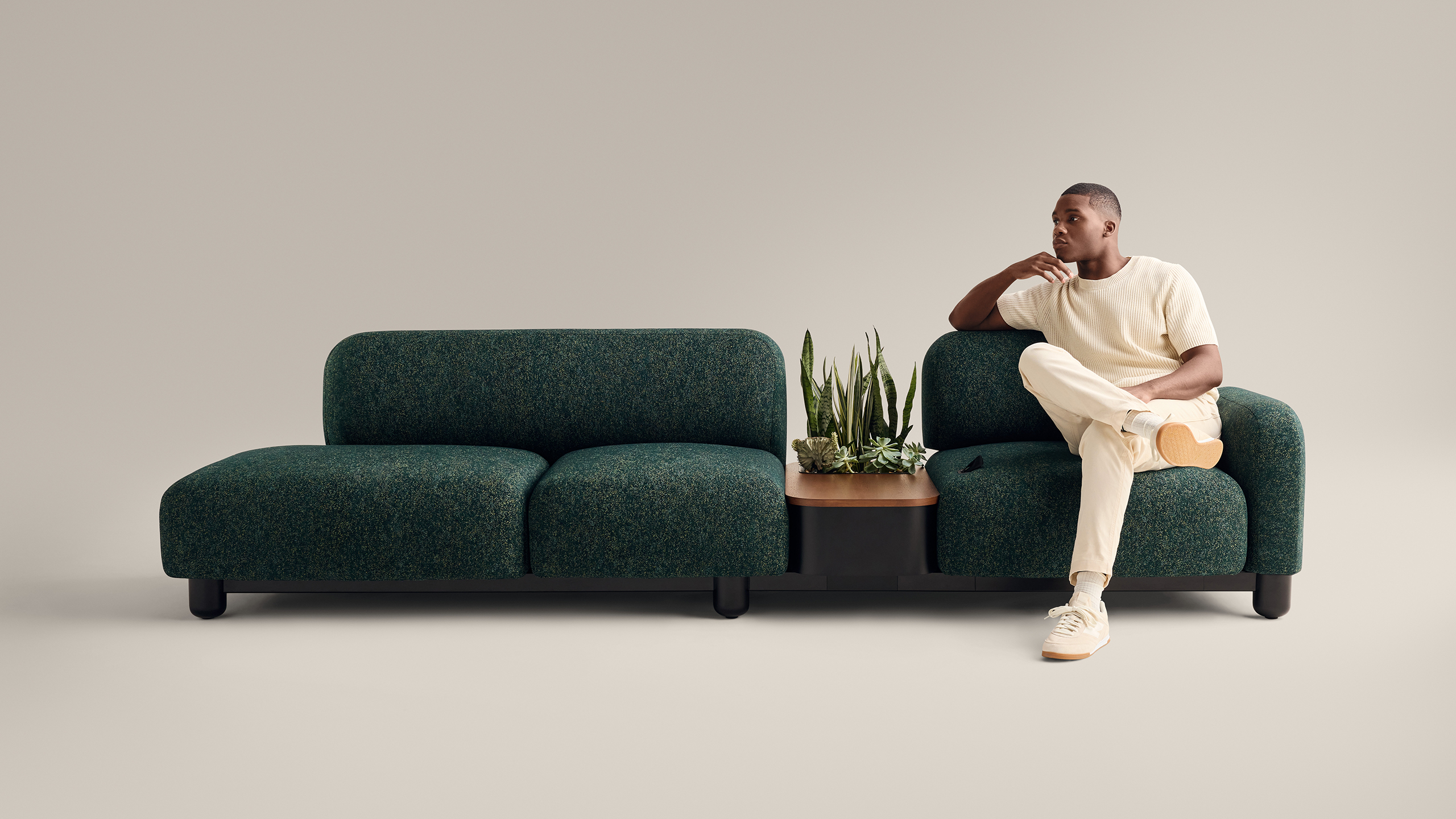 front view of a man sitting comfortably in an emerald green Coalesse Ensemble Lounge sofa