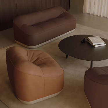 Brown lounge chairs and a matching sofa arranged around a round black coffee table in a modern living space.