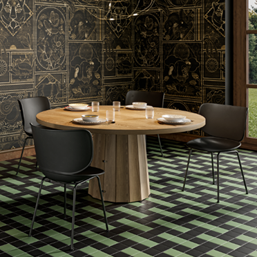 Round wooden dining table set with tableware, surrounded by four black chairs in room with patterned floor and decorative wall.