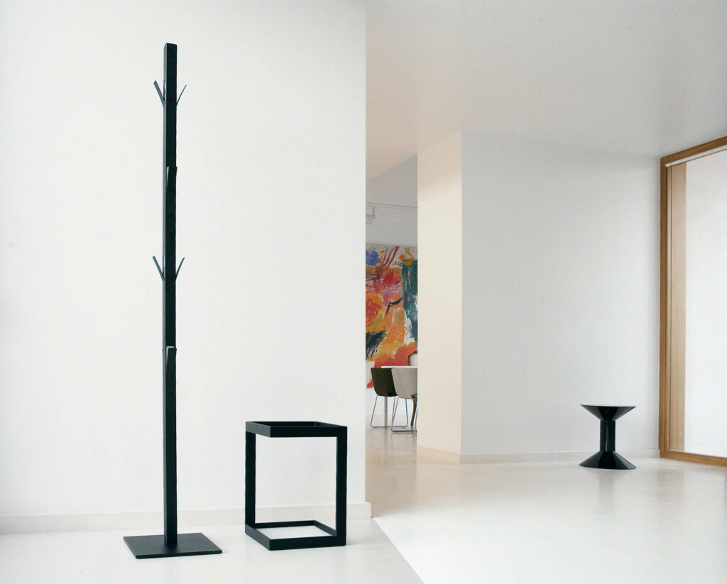 Coat Rack next to a mini table in an all-white room with a colorful painting in the background.