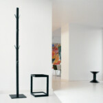 Coat Rack next to a mini table in an all-white room with a colorful painting in the background.
