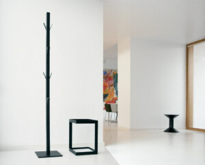 Coat Rack next to a mini table in an all-white room with a colorful painting in the background.